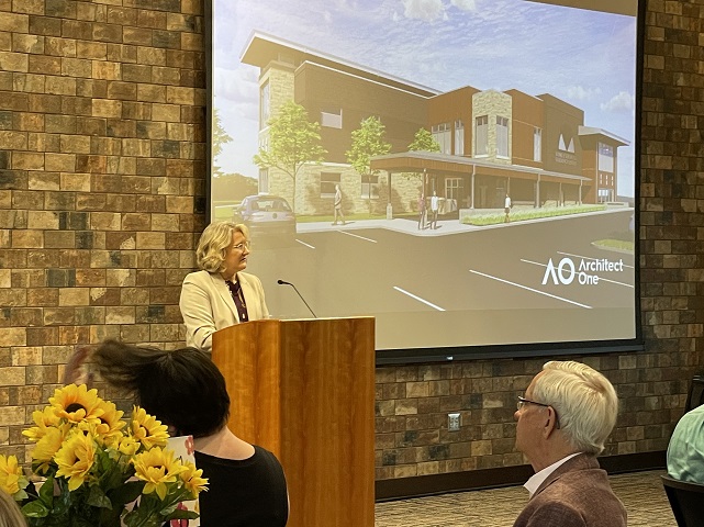 An FSGC Staff Member Stands At Podium. She stands in front of projector screen that shows digital art of a new building. The art is labeled Architect One in the Corner.