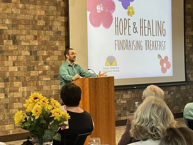 An FSGC Male Staff Member Stands At Podium and Speaks to Seated Audience at the Hope & Healing Fundraising Breakfast.