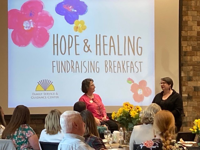 A female FSGC Staff Member and Success Story Mother Stand At Front of Room At Hope & Healing Fundraising Breakfast.
