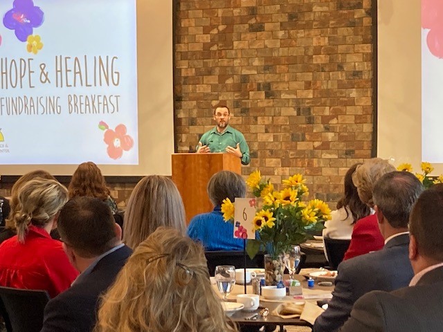 An FSGC Staff Member Speaks to Audience From Podium At Hope & Healing Fundraising Breakfast.