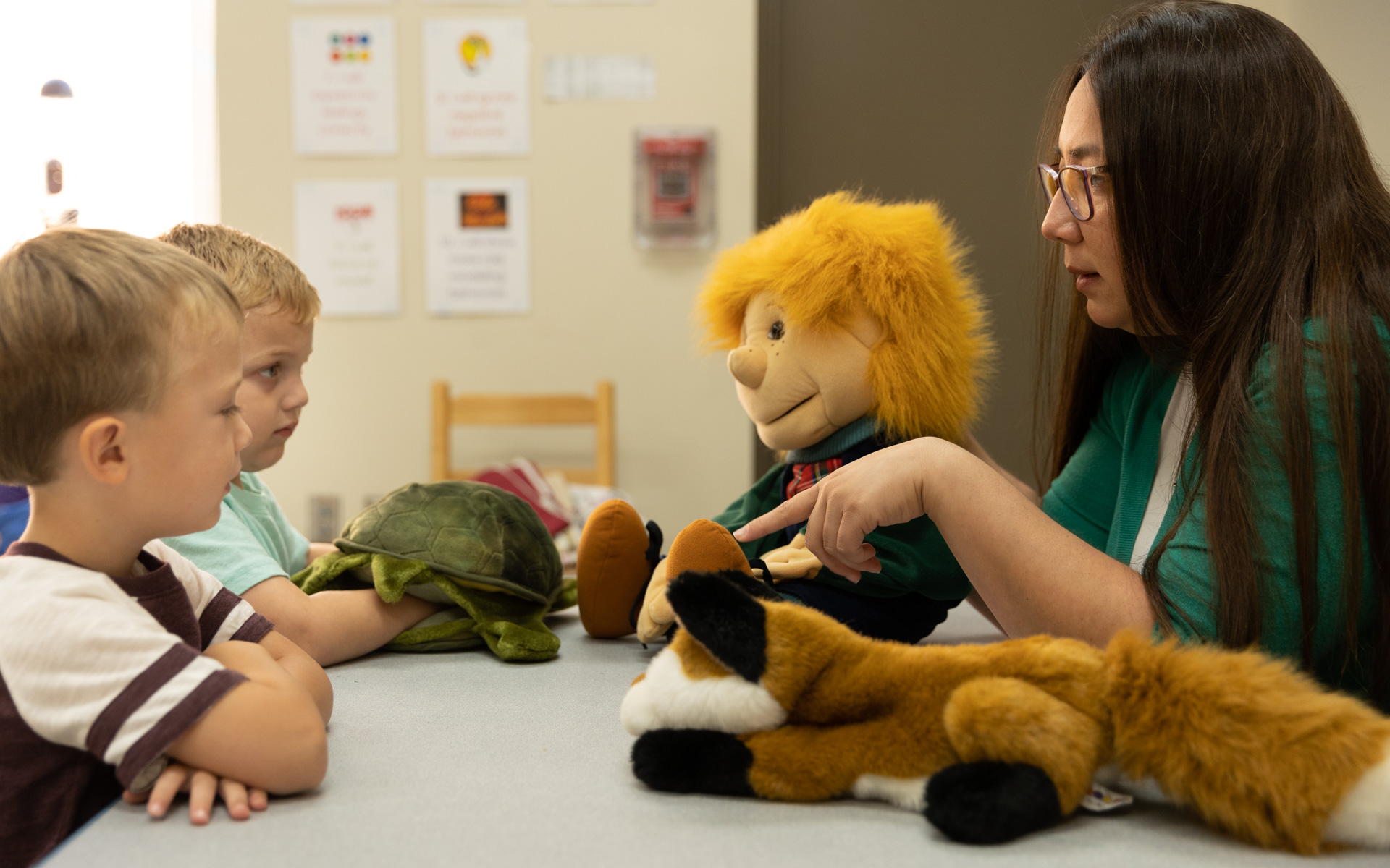 Female staff member uses stuffed animal to do the Happy Bear presentation for two young boys