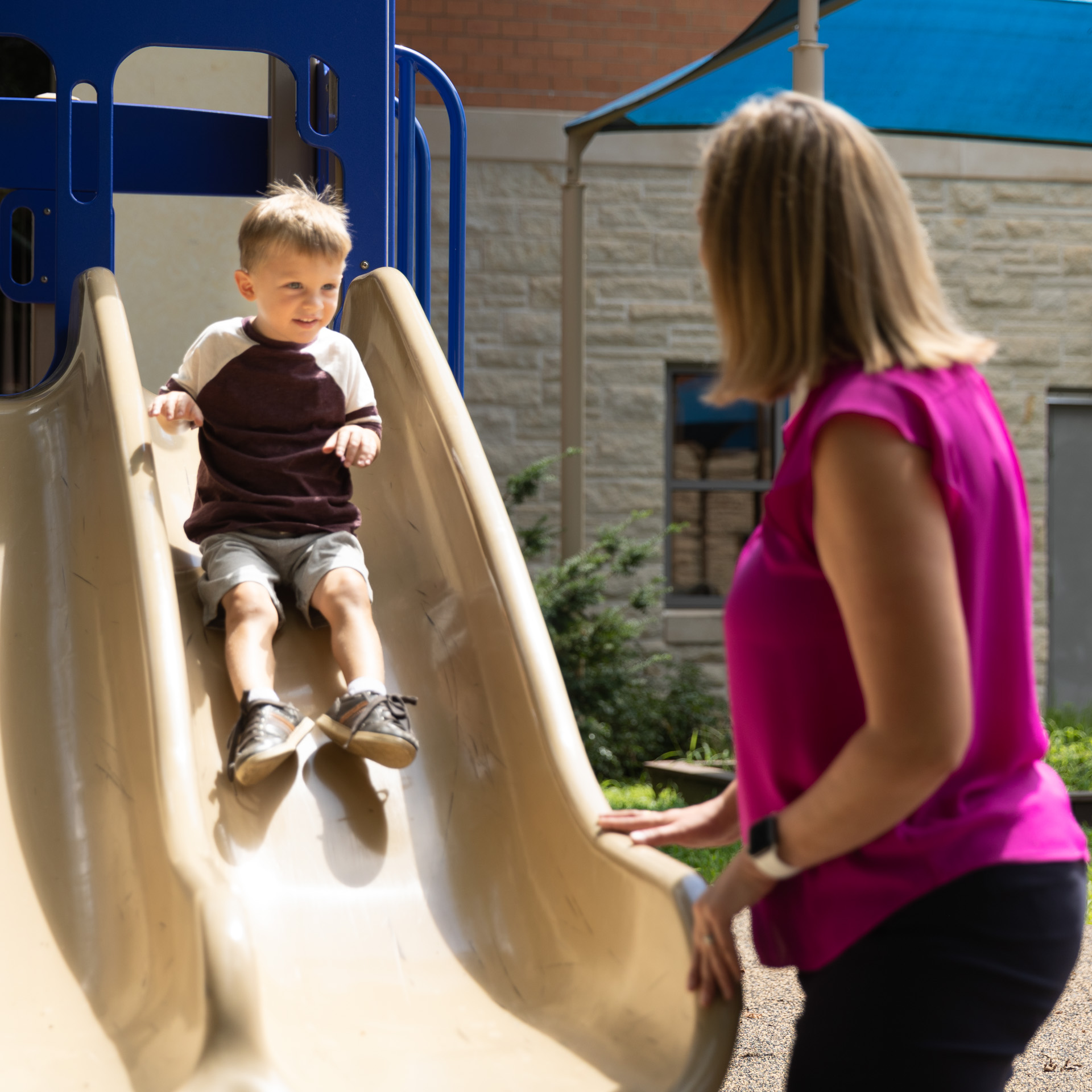 Women helping little boy go down the slide at a playground