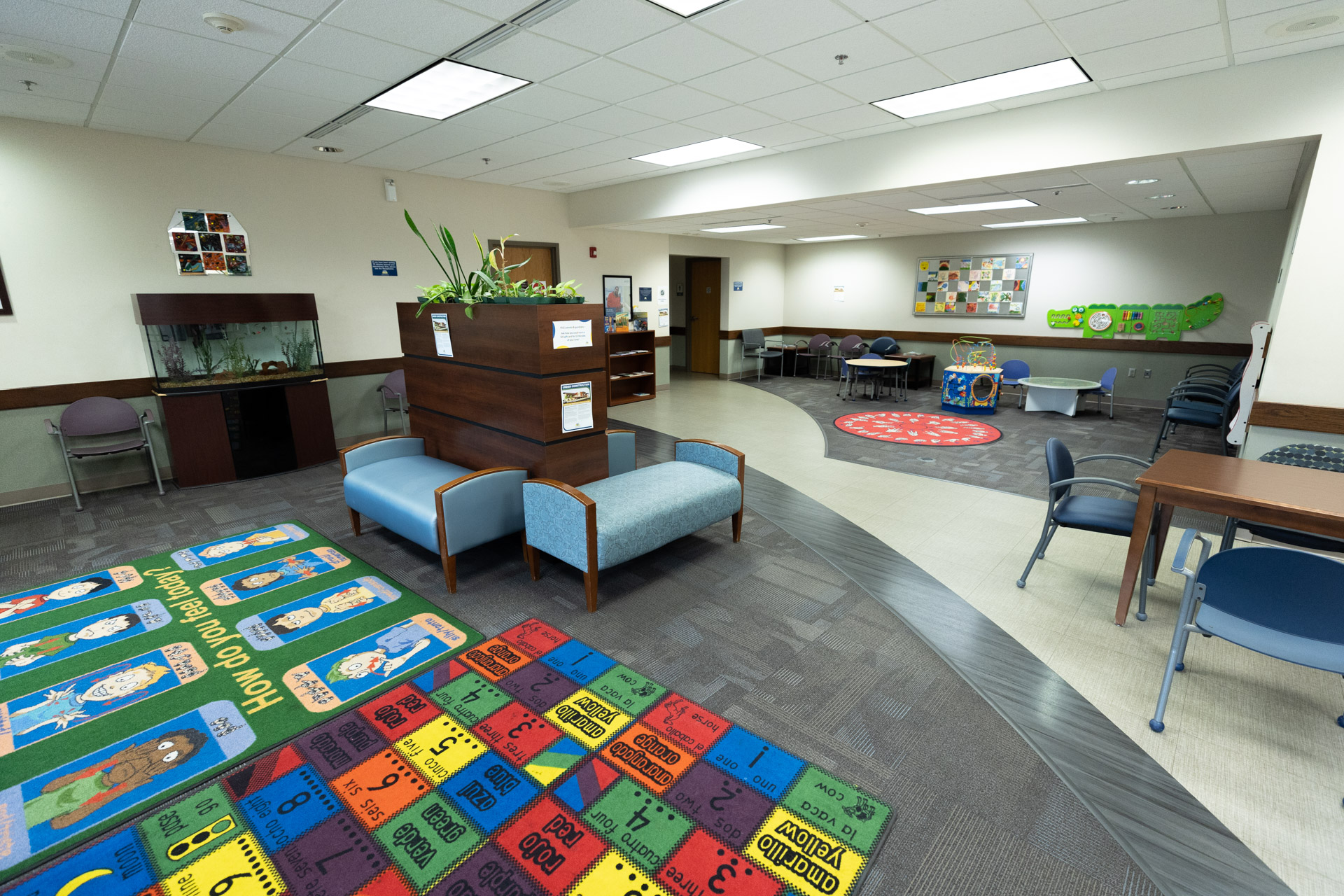 Interior lobby. Multiple patterned rugs are on the ground with lots of seating options. Several tables with toys for children.