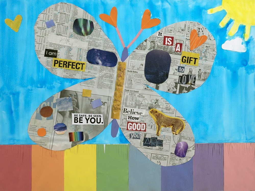 A collaged piece of artwork. A butterfly made out of newspaper is glued on top of a piece of paper with a watercolor sun and sky, and rainbow pieces of paper at the bottom of the page. In various fonts, words are glued onto the butterfly's wings: I Am Perfect. Be Safe. Be Seen. Be You. Believe How Good You Are. It Is A Gift To Love.