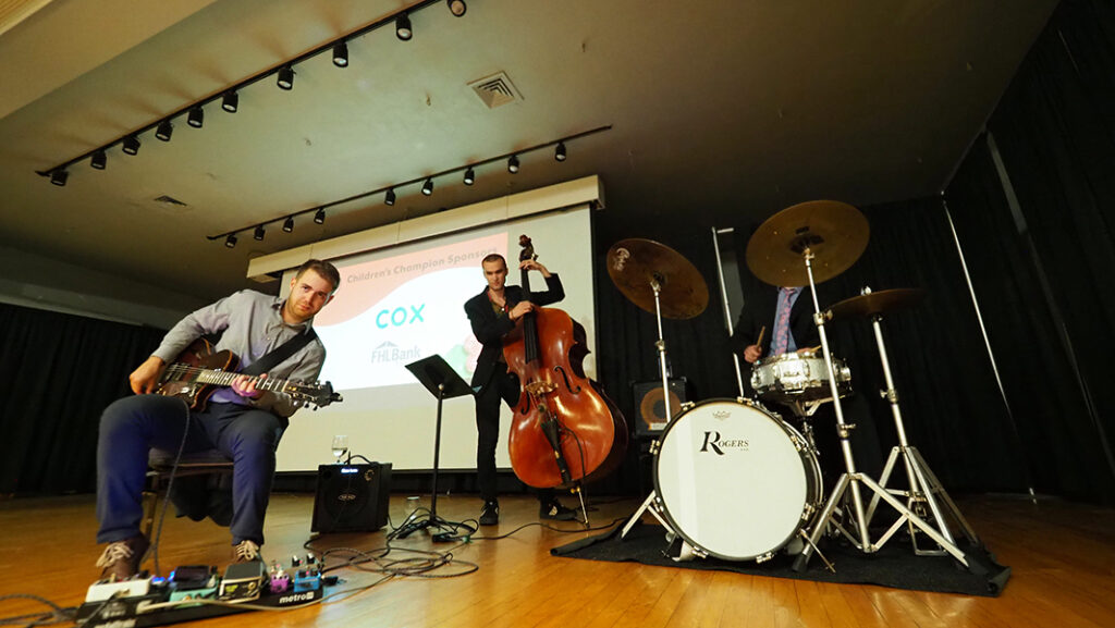 A band plays on stage in the room with the silent auction. There is a guitar, bass, and drum set.