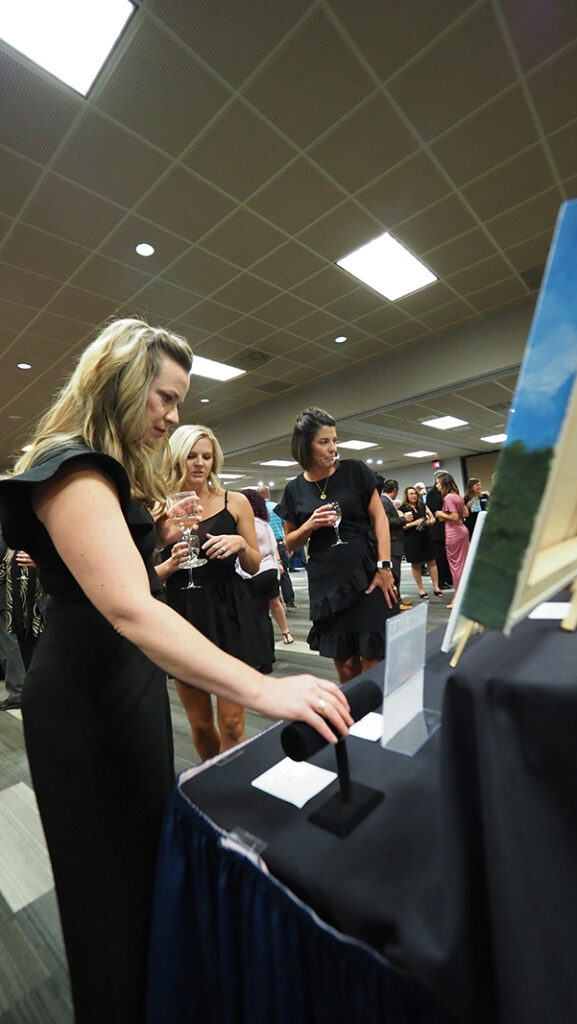 The silent auction room is filled with people looking at items displaced on tables.