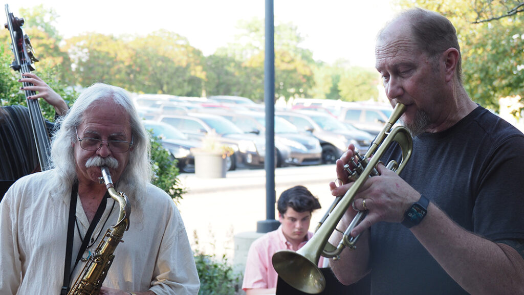 A male with a saxophone and a male with a trumpet play outside.