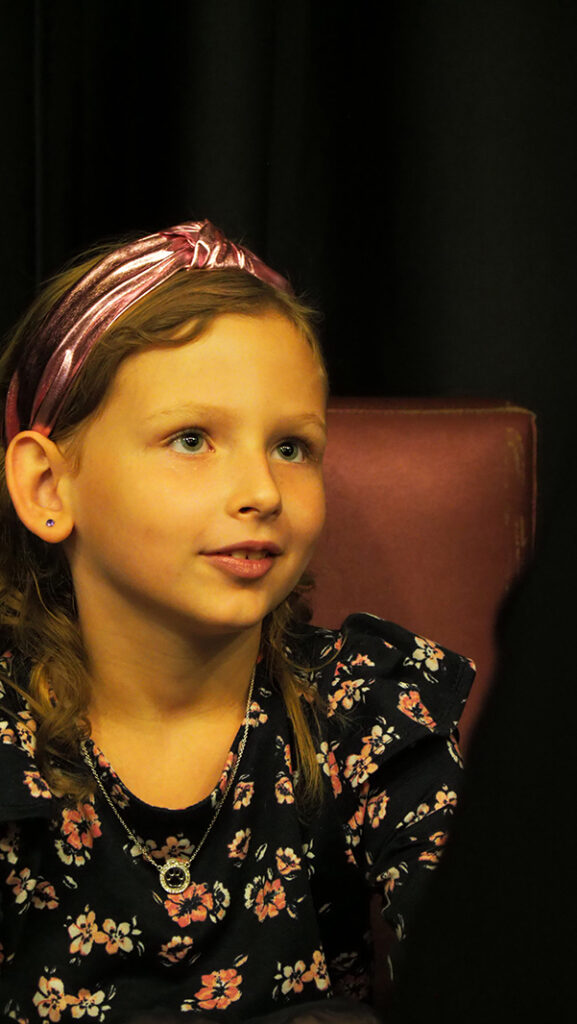 A young female featured artist in a pink headband and a dress with a floral top.