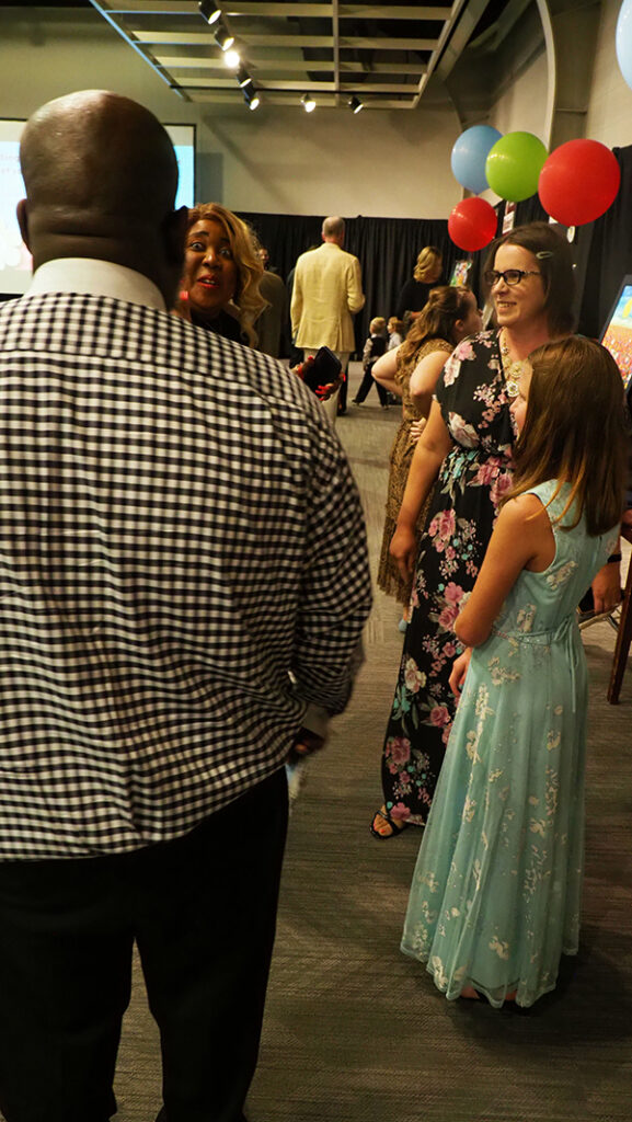 A young female featured artist in a light blue dress stands and talks to three adults.