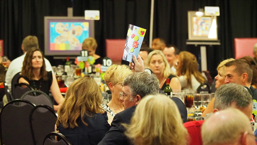 A male guest hold up his bidder number in the middle of a crowded room.