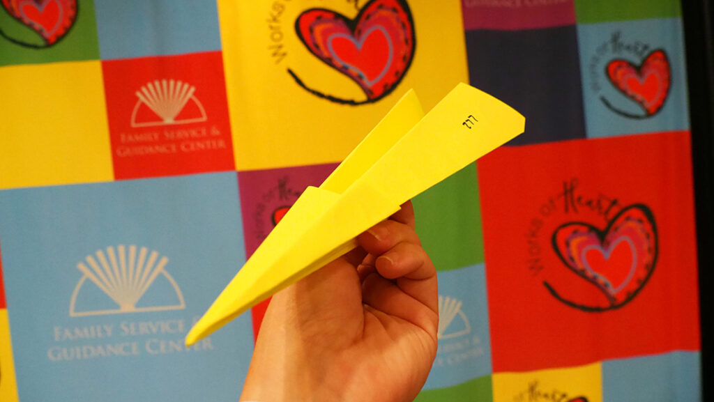 Neon yellow airplane folded out of paper for the paper airplane challenge.