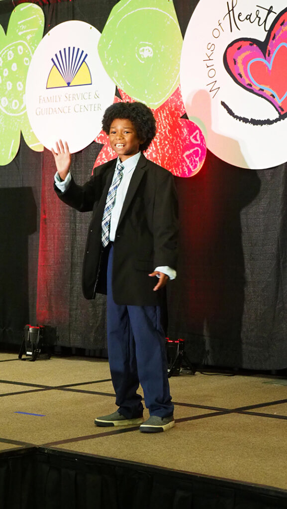 A young male featured artist with a tie and suit jacket waving on stage.