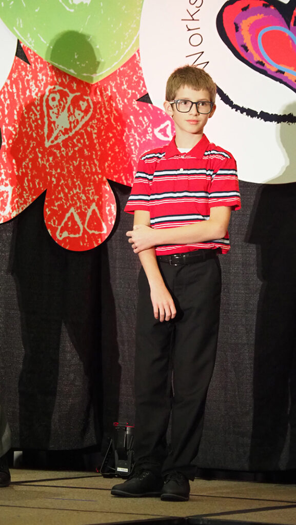 A young male featured artist with glasses and a striped polo shirt standing on stage.